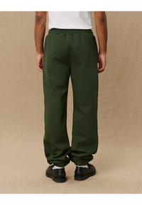 Green sweatpants with elastic waistband, snug ankle cuffs, and side pockets. Smooth fabric texture, designed for comfort and ease of movement.