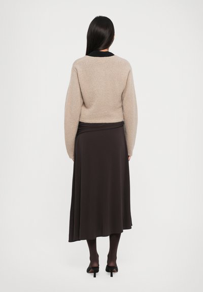 Beige cropped sweater with a soft texture, paired with a long brown skirt. The look is completed with dark tights and black heeled shoes.