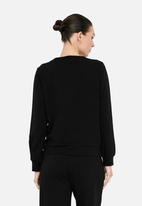 Zwarte sweatshirt met lange mouwen, ronde hals, ribbelmanchetten en onderkant. Zachte stof met een gladde textuur. Draagt met bijpassende zwarte broek.