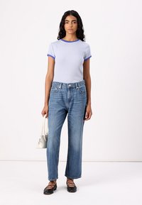 Camisa de manga curta às riscas azul e branca com colarinho canelado, combinada com jeans de perna reta azul claro. Segurando uma pequena bolsa branca.