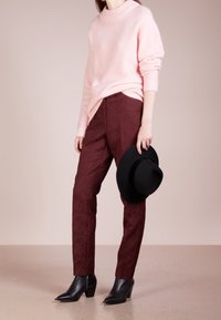 Ljusrosa stickad tröja, vinröda mönstrade byxor, svarta ankelboots och en svart filthat. Släta texturer med en avslappnad passform.