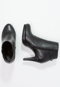 Schwarze Lederstiefeletten mit einem zulaufenden Absatz und einem seitlichen Reißverschluss. Sie verfügen über eine glatte Textur und subtile Nietenverzierungen in der Nähe des Reißverschlusses.
