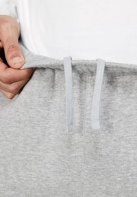 Grå mjukisbyxor med dragsko i midjan; mjuk struktur; elastiska fotleder; närbild som framhäver sömmar och tygdetaljer.