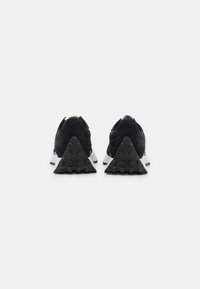 Schwarze Sportschuhe aus Mesh und Wildleder. Merkmale sind ein markanter dreieckiger Absatz aus strukturiertem schwarzem Gummi und dezente weiße Akzente.