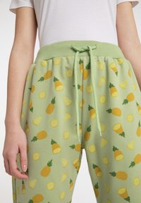 Grüne Sweatpants mit einem sich wiederholenden Muster aus gelben Ananas und Zitronenscheiben, mit einem Kordelzugbund und weichem Stoff.ಉ