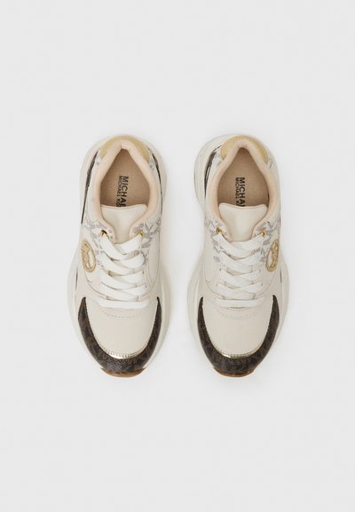 Zapatillas blancas y beige con parte superior de tela texturizada, acentos dorados y un panel marrón con patrón en la puntera. Diseño con cordones y cuello acolchado.