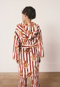 Accappatoio con cappuccio a righe rosse e bianche con motivi di omini di pan di zenzero, realizzato in tessuto morbido e peluche. Stile con vita annodata e pantaloni coordinati.