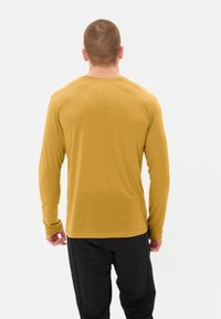 Chemise à manches longues en jaune moutarde, tissu doux, col rond, design ajusté, coutures visibles, associée à un pantalon noir.