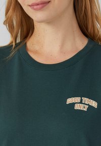 Sweat-shirt en coton vert avec un col rond et un texte brodé beige clair qui indique "BON MOMENTS UNIQUEMENT" à l'avant.