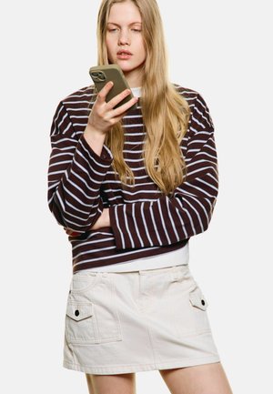 Brown and light blue striped long-sleeve shirt, layered over a white top, paired with a light beige skirt featuring side pockets.