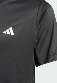 Czarna sportowa koszulka o gładkiej fakturze, z białym geometrycznym logo na lewej piersi oraz krótkimi rękawami w luźnym kroju.