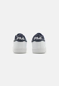 Vita sneakers med en slät, texturerad finish, marinblå accenter vid hälen och en framträdande "FILA"-logotyp på baksidan. Lågdesign.