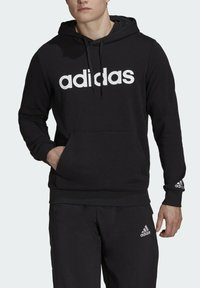 Felpa nera in misto cotone, con grande logo bianco "adidas", tasca a marsupio, polsini a coste e texture morbida.