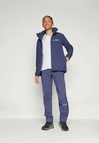 Tamsiai mėlynas Terrex striukės ir kelnių komplektas, turintis užtrauktuko priekį, elegantišką dizainą, lengvą medžiagą ir logotipo akcentus ant krūtinės ir kojos.