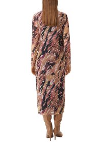 Langes, durchscheinendes Kleid mit einem mehrfarbigen abstrakten Muster in Pink, Braun und Schwarz. Kombiniert mit beigefarbenen kniehohen Stöckelschuhen.