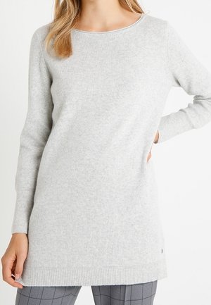 Femme portant un pull en maille gris clair à manches longues avec un col rond et un pantalon gris à carreaux.