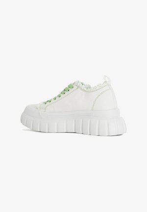 Sneakers bianchi in tela con un design semplice, caratterizzati da occhielli verdi, un orlo in frange texturizzato sul collo e una suola in gomma bianca spessa.