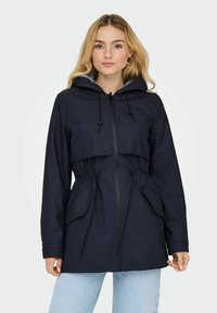 Veste imperméable marine avec capuche, taille ajustable et deux poches avant. Dispose d'une fermeture éclair et d'une doublure intérieure rayée.