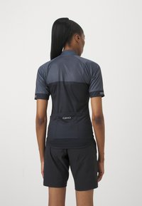 Maillot de cyclisme à manches courtes en gris foncé, avec des panneaux en mesh, une coupe ajustée et un logo Giro dans le bas du dos. Associé à un short noir.