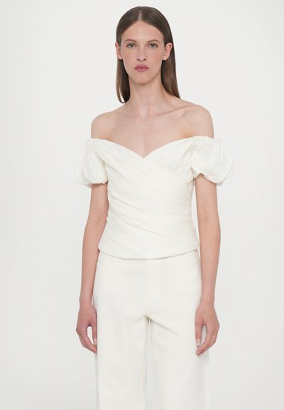 Off-the-shoulder white top with puff sleeves, ruched texture, and a fitted bodice. Paired with light, wide-leg trousers.