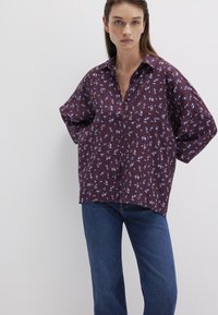 Burgundy button-up shirt with a floral pattern in light blue, featuring a relaxed fit and wide sleeves, paired with dark blue jeans.