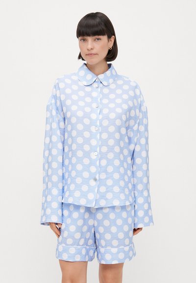 Ensemble de pyjama à pois bleus clairs avec une chemise à col et un pantalon court assorti. Le tissu a une finition texturée avec des motifs circulaires blancs.