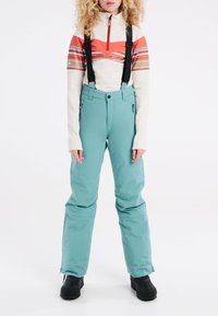 Sneeuwbroek in teal met verstelbare zwarte banden, gecombineerd met een crèmekleurige en rode zip-up top met horizontale strepen. Dikke en geïsoleerde ontwerp.