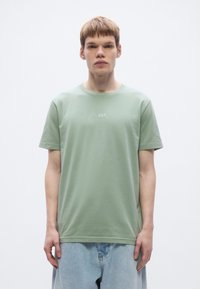 Light green cotton t-shirt with short sleeves, round neckline, and embroidered "BOSS" logo at chest. Paired with light denim shorts.