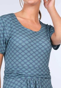 Ein blaues und grünes gemustertes Kleid mit runder Ausschnittlinie und kurzen Ärmeln, das ein florales Design auf dunklem Hintergrund zeigt. Weiche Stofftextur.