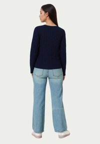 Pulover bleumarin cu model tricotat în relief și mâneci lungi, asortat cu blugi evazați de culoare albastru deschis. Ținuta este completată de adidași cu platformă în nuanțe deschise.