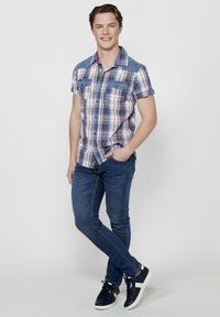 Camicia a maniche corte a scacchi blu, rossa e bianca con spalle in denim; abbinata a jeans slim-fit blu e sneaker blu navy.