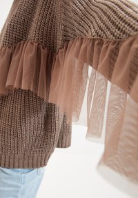 Brązowy sweter z dzianiny o fakturowanym wzorze, z falbaniastą narzutą z tiulu w jaśniejszym brązie, tworzącą warstwowy efekt wizualny.