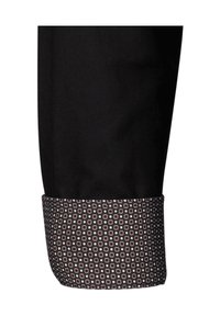 Schwarze Stoffhose mit einem gemusterten Saum, der geometrische Formen in Beige und Marineblau zeigt, und einen Kontrast zwischen einfarbigen und gemusterten Bereichen hervorhebt.