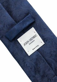 Laivastonsininen kangassolki, jossa on kulutettu paisley-kuvio. Ompeleva tarra, jossa lukee "JOHN HENRIC, RUOTSI, Valmistettu Italiassa." Tasainen, elegantti viimeistely.