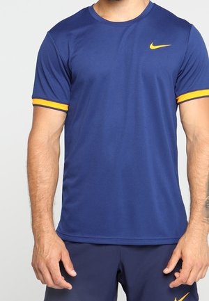 Mężczyzna w niebieskiej sportowej koszulce Nike z żółtymi wykończeniami na rękawach i żółtym logo Nike na piersi, do tego niebieskie spodenki.