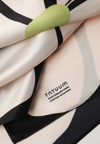 Foulard di seta con uno sfondo rosa chiaro e motivi astratti neri e verdi. L'etichetta riporta "tntuum" e include dettagli sul copyright.