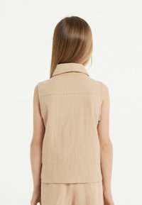 Beige mouwloze blouse met een kraag en een textured stof; strakke lijnen met een rechte snit aan de zoom.