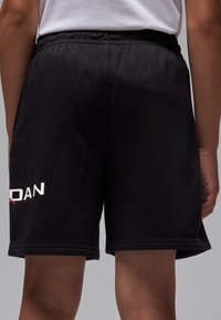 Schwarze Sportshorts aus weicher Baumwolle, ausgestattet mit einem elastischen Bund und einem weißen Logo am linken Bein.