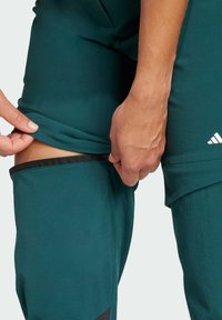 Teal athletic pants with a zippered side for adjustable length, featuring elastic waistband and black accents near the hem.