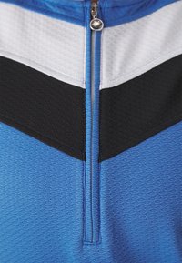 Μπλε αθλητικό μπλουζάκι με φερμουάρ στον λαιμό, υφασμάτινη επιφάνεια, με μαύρες και άσπρες ρίγες στους θωρακικούς και ώμους.