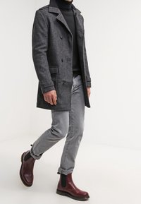 Cappotto lungo in misto lana grigio con frontale doppiopetto, spalline e due tasche laterali. Abbinato a jeans grigi chiari e stivaletti malva.