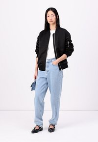 Fekete bomber dzseki, fehér textúrájú felső, világoskék, magas derekú farmernadrág, fekete slip-on cipők fehér akcentussal. Minimalista dizájn, laza szabás.