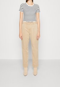 Femme portant un pantalon beige à jambes droites avec ourlets retroussés, un t-shirt à manches courtes blanc et noir à rayures, et des bottes beige à bout pointu.