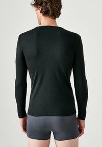 T-shirt noir à manches longues en tissu doux, ajusté. Associé à un short de boxeur gris, montrant une texture et des coutures lisses.