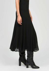 Robe midi noire avec une silhouette fluide, en tissu transparent, et détail en dentelle au niveau du col, associée à des bottes en cuir noir à talons bloc arrivant au genou.