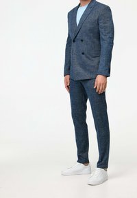 Niebieska, teksturowana marynarka dwurzędowa połączona z dopasowanymi spodniami i białymi trampkami. Strój uzupełnia prosta koszulka z okrągłym dekoltem.