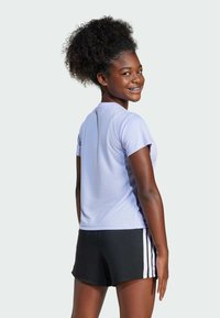 Camiseta atlética de color púrpura claro hecha de una tela texturizada, combinada con pantalones cortos negros con franjas blancas a los lados.