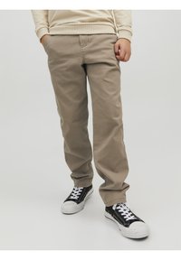 Beiga bomullschinos med rak passform, som har sidofickor och en avslappnad stil, tillsammans med svartvita sneakers.