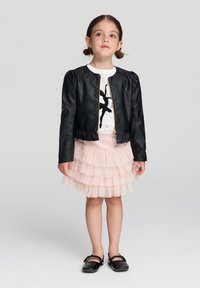 Czarna kurtka z imitacji skóry z puszystymi rękawami i falbanką, noszona na białej bluzce z czarną sylwetką baletnicy. Jasnoróżowa, warstwowa spódnica z tiulu.