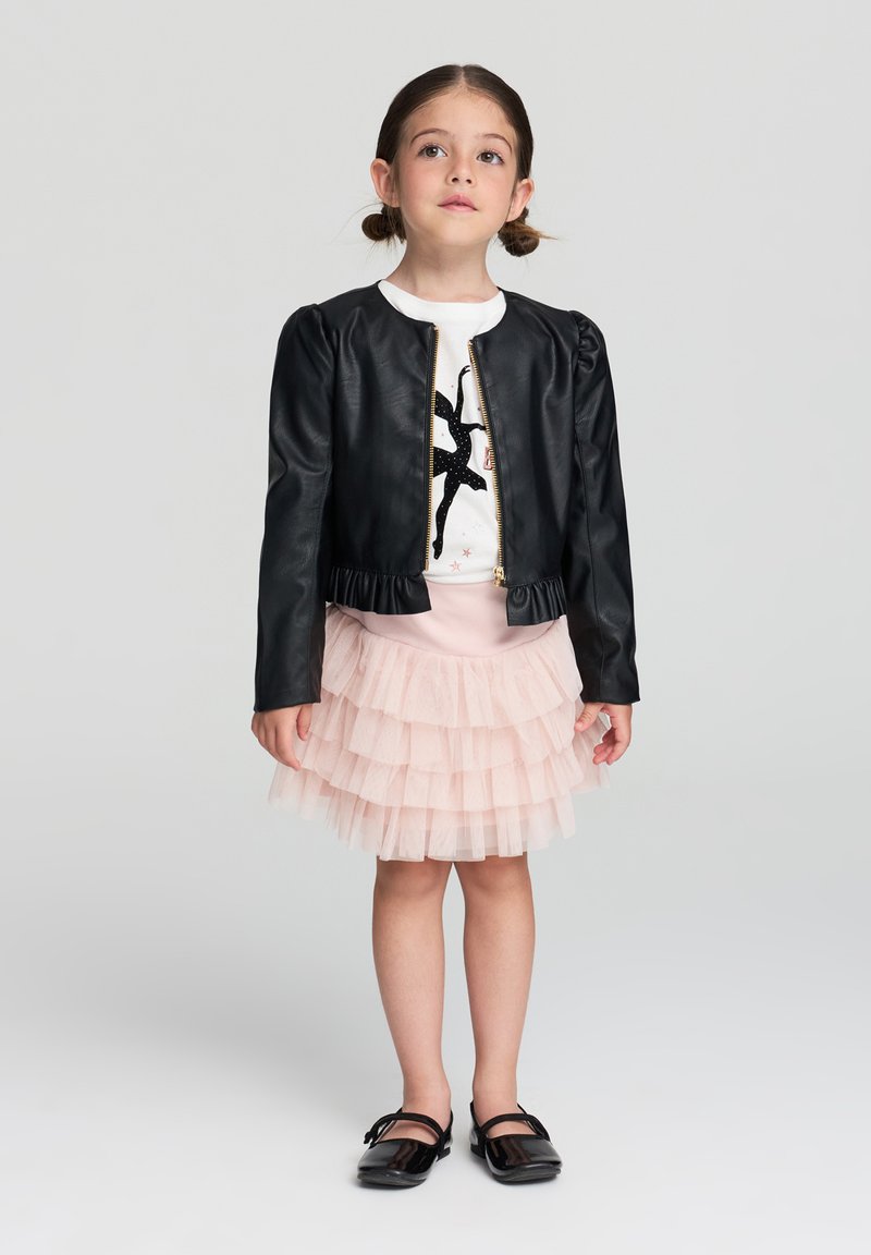 Czarna kurtka z imitacji skóry z puszystymi rękawami i falbanką, noszona na białej bluzce z czarną sylwetką baletnicy. Jasnoróżowa, warstwowa spódnica z tiulu.